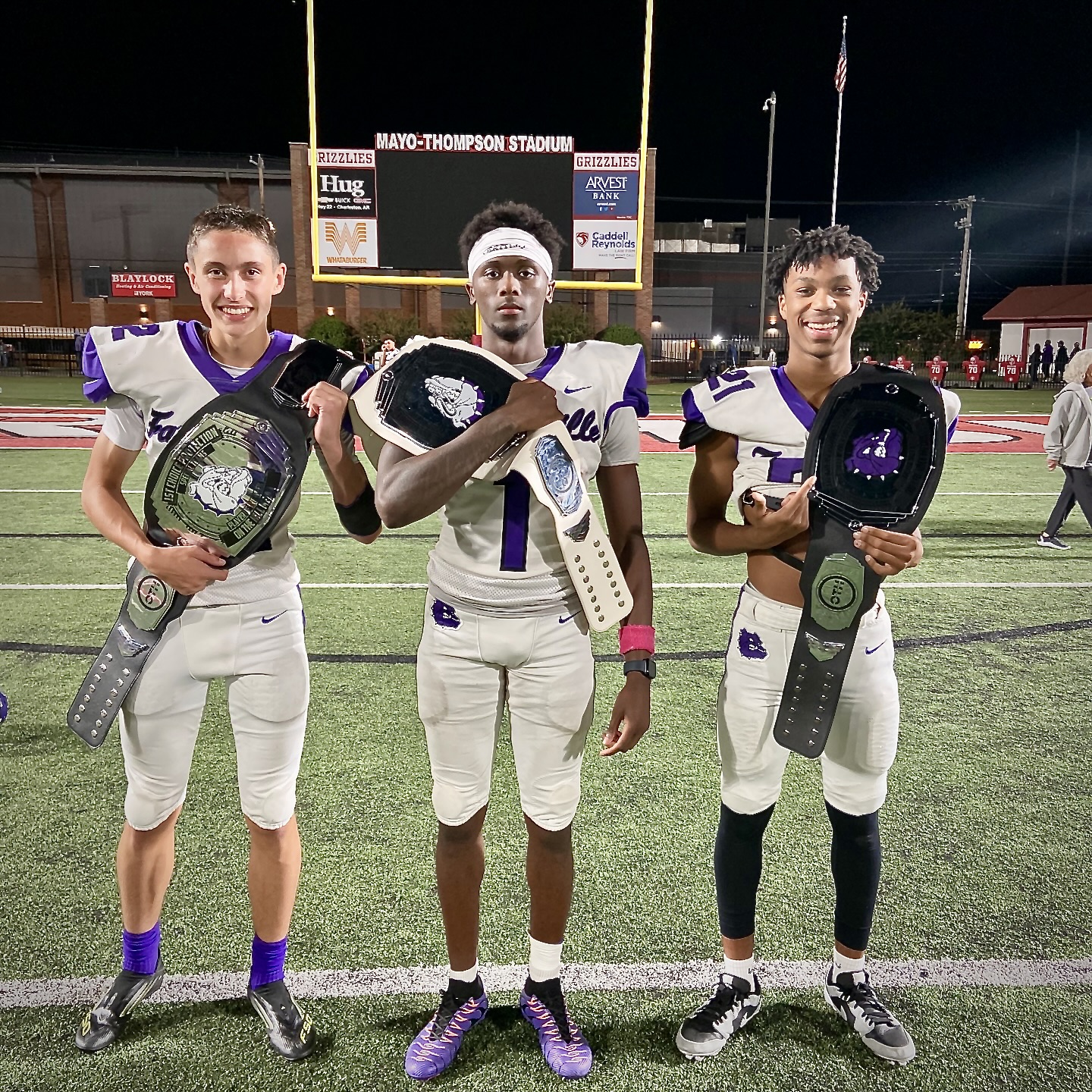 Ethan Farthing standing with teammates on the field holding player-of-the-week championship-style belts.