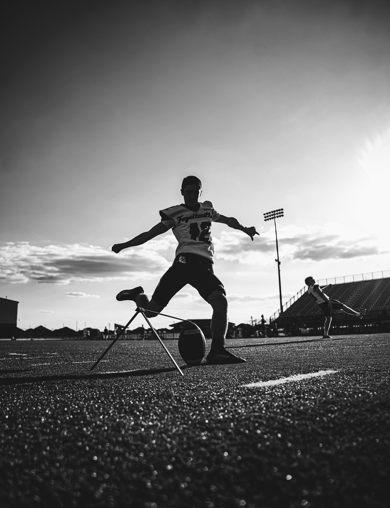 Black-and-white low-angle silhouette of Ethan Farthing approaching the ball on a tee during practice.