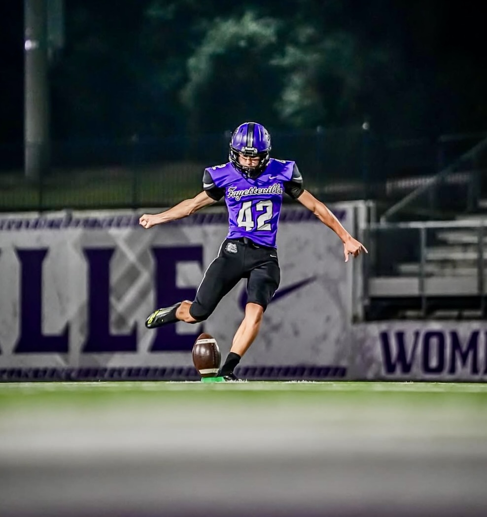 Ethan Farthing, number 42, striking a kickoff for Fayetteville High School under the lights.