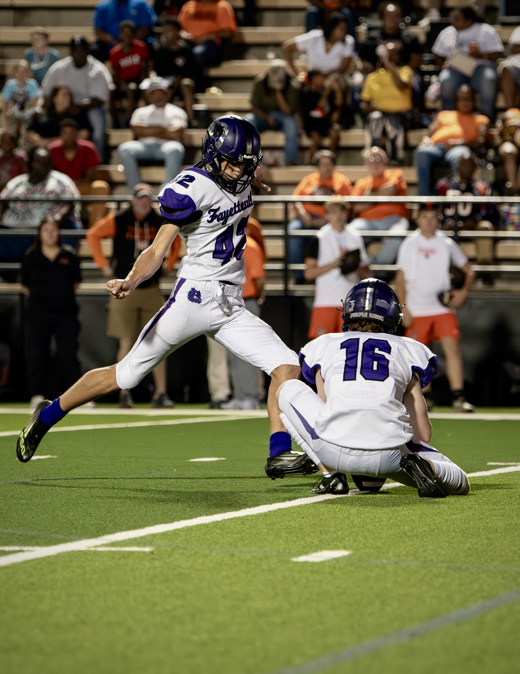 Ethan Farthing striking a Varsity placekick with his holder set in front of him.